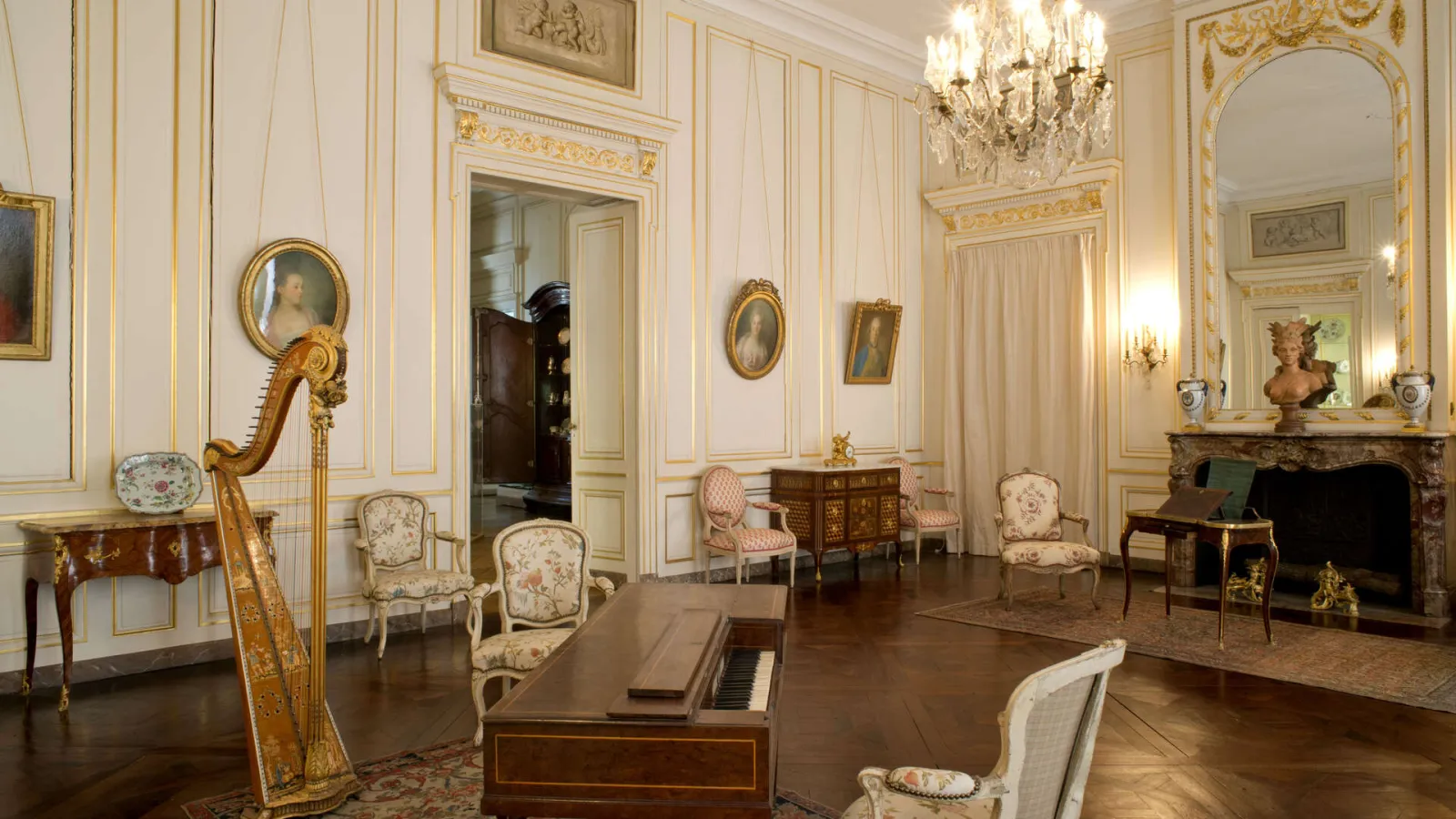 Rococo drawing room in the Bordeaux Museum of Decorative Arts and Design featuring white and gold paneling, period furniture, golden harp, oval portraits, fireplace and crystal chandelier