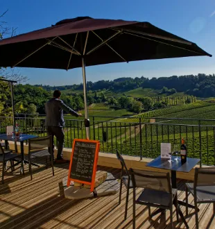 Sunny terrace at Château La Croizille with black umbrella, tables and chairs overlooking Bordeaux vineyards
