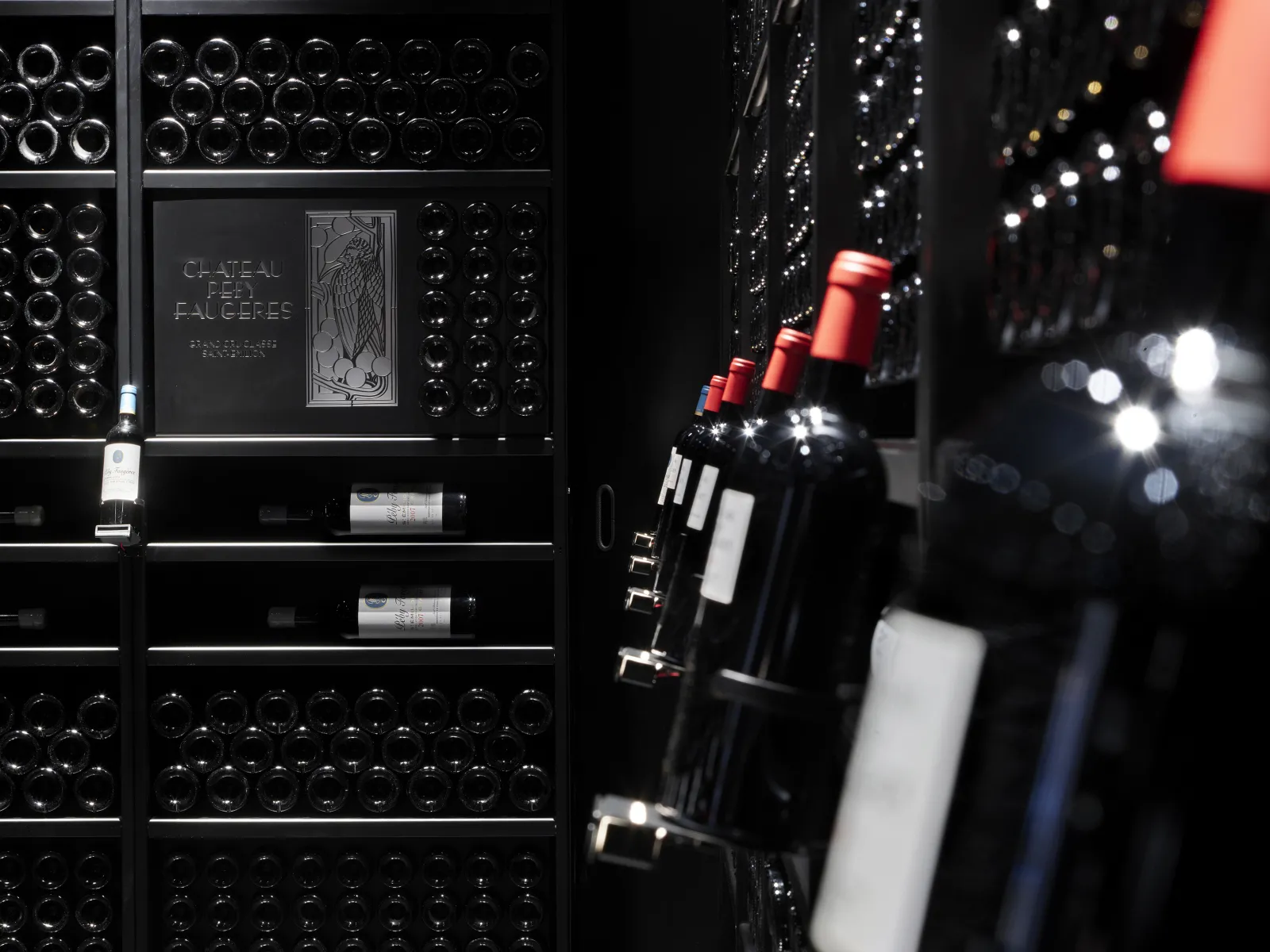 Wine cellar at Château Peby Faugères in Bordeaux featuring wine bottles stored on black shelves with visible labels