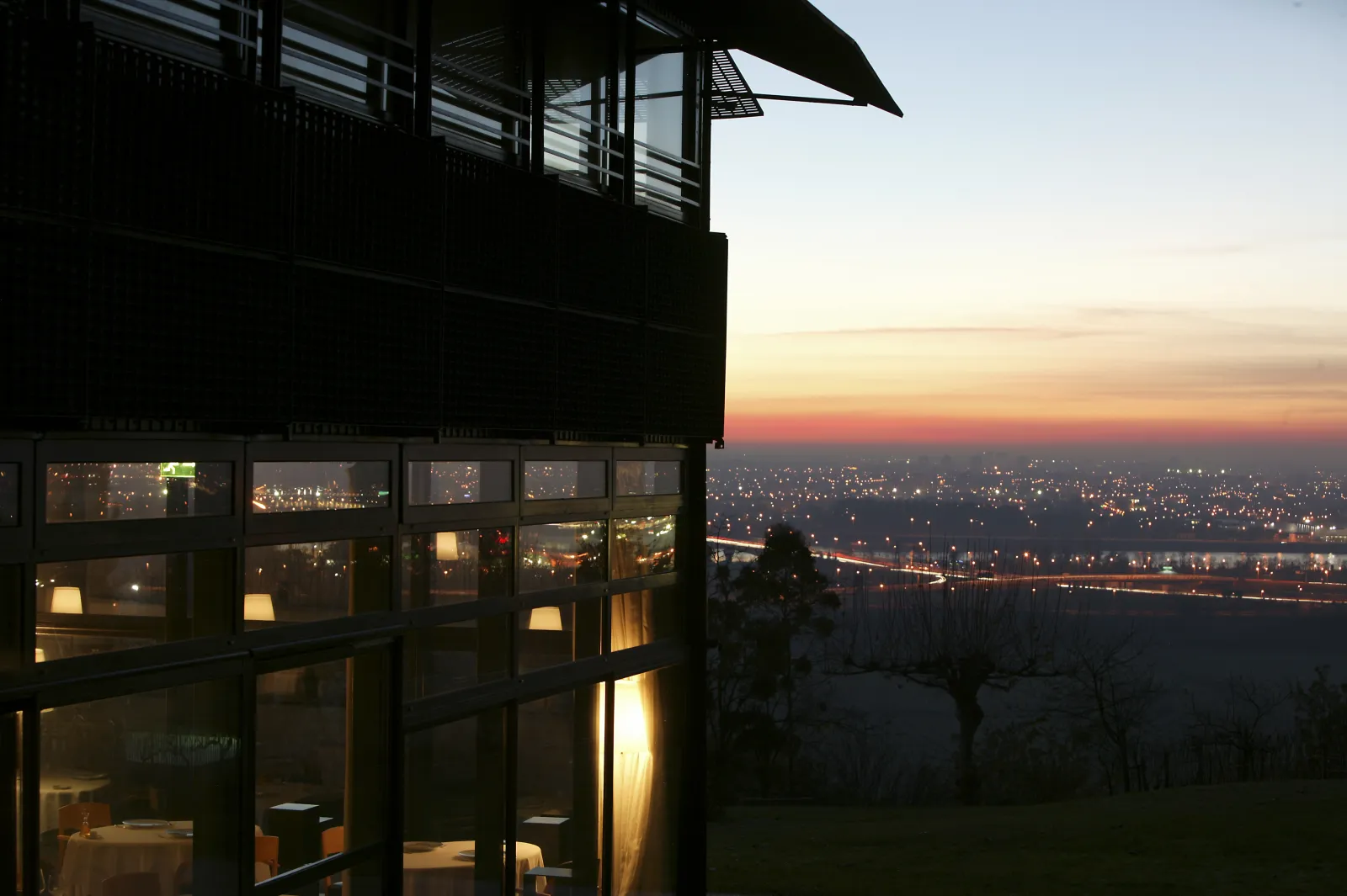 Night view from Le Saint-James hotel in Bordeaux: modern building with illuminated glass facade overlooking the twinkling city at sunset, with the Garonne river and its lights in the background.
