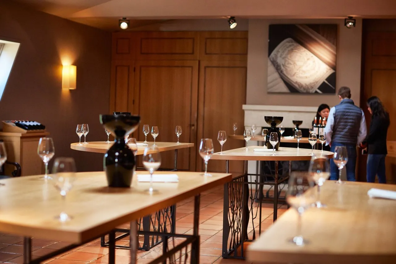 Elegant tasting room at Château Pichon Baron in Bordeaux featuring wooden tables, wine glasses and modern décor, with three people in the background