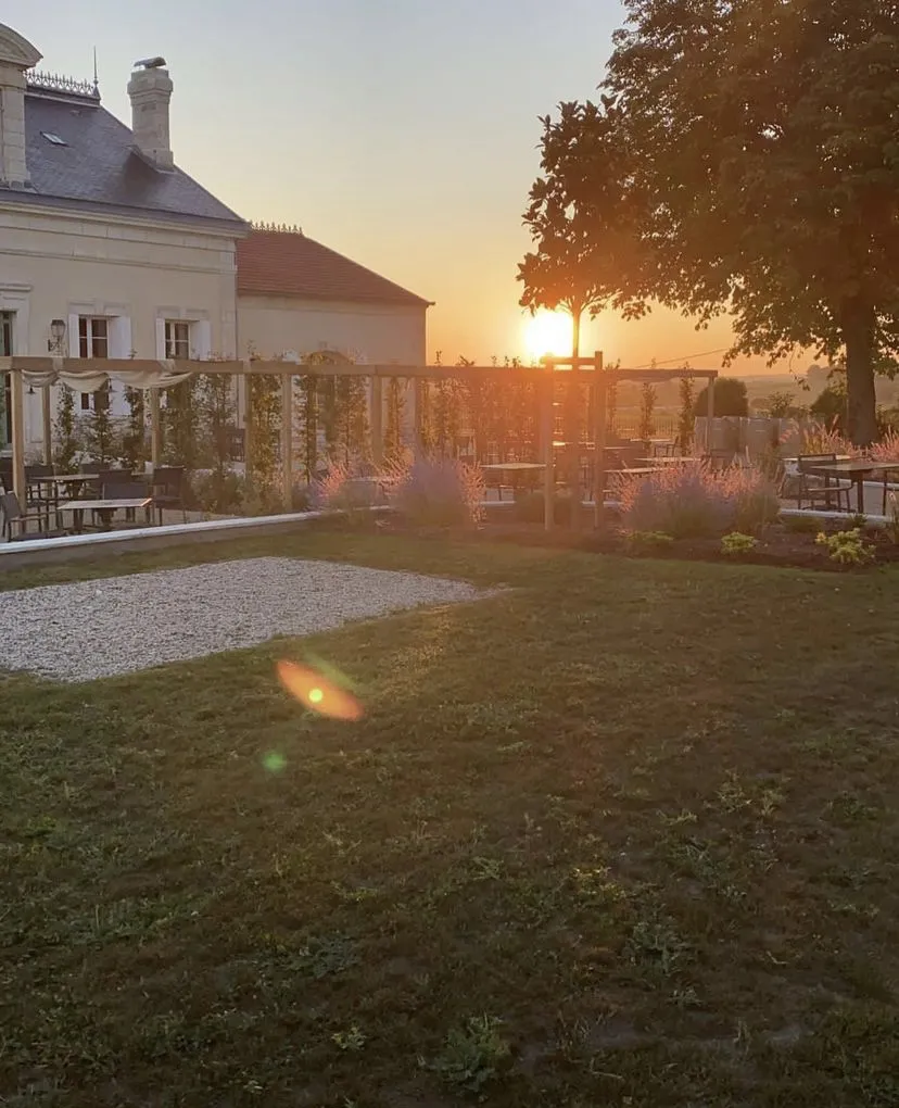 Sunset view of Jardin à Petit Faurie de Soutard in Bordeaux, featuring a white house, wooden terrace, plantings and a large tree on the right