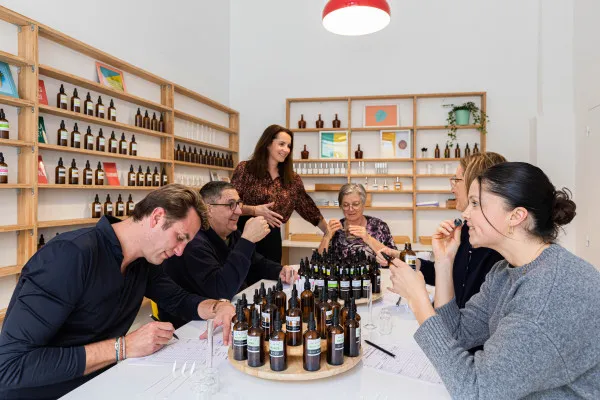 Five people participate in an olfactory tasting session in a studio in Bordeaux, gathered around a table with fragrance bottles and tasting notes, with wooden shelves of products visible in the background.