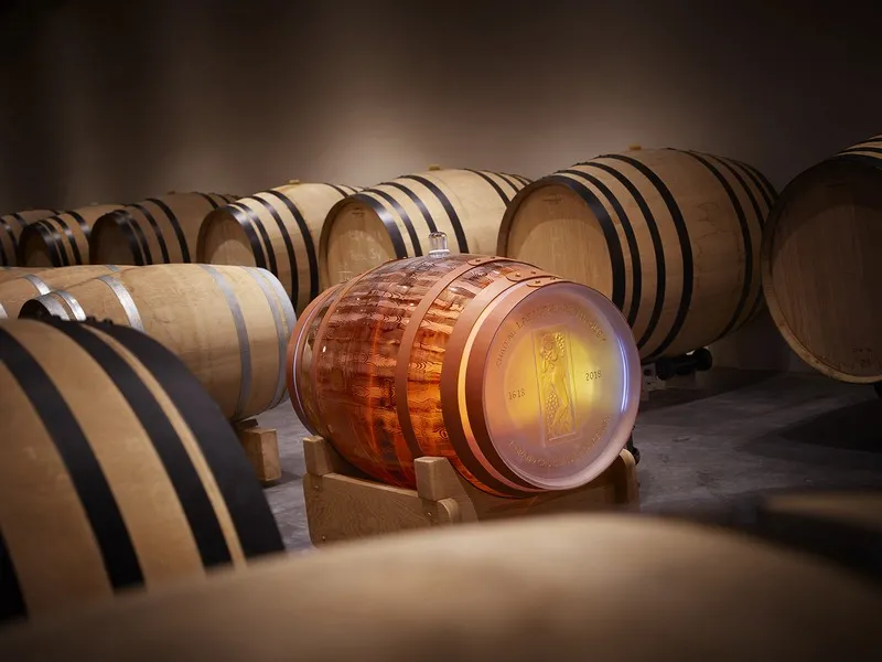 Row of oak barrels in a Bordeaux château cellar, with a glowing barrel in the foreground containing red wine and multiple barrels lined up in the background.