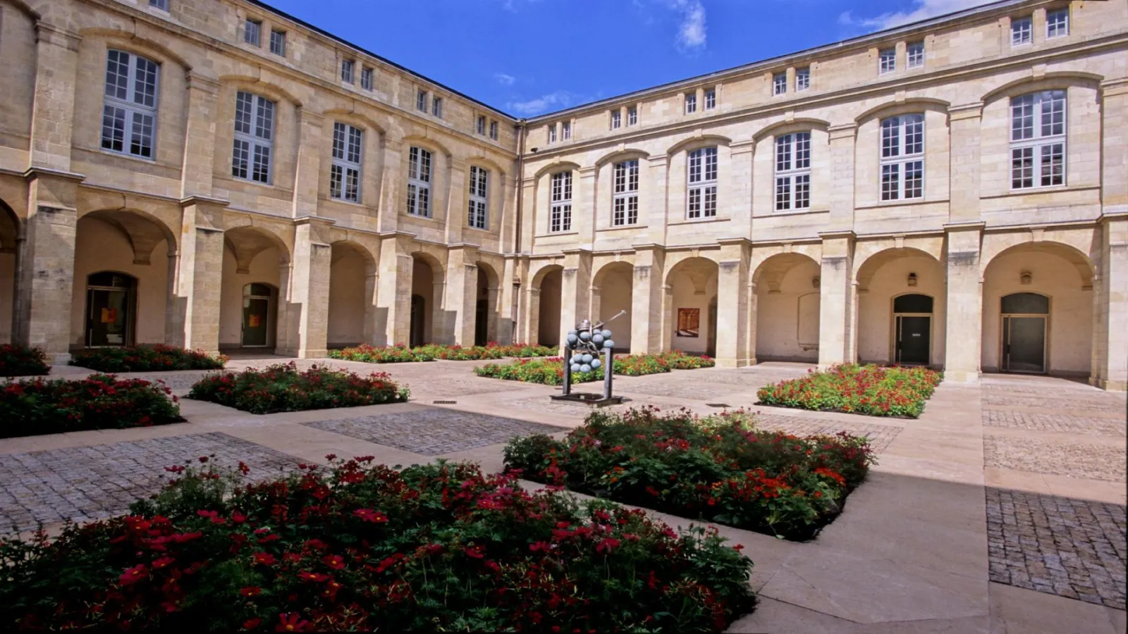 Mably Courtyard in Bordeaux featuring stone arcades, red flowering plants, and central sculpture with classical 18th-century architecture