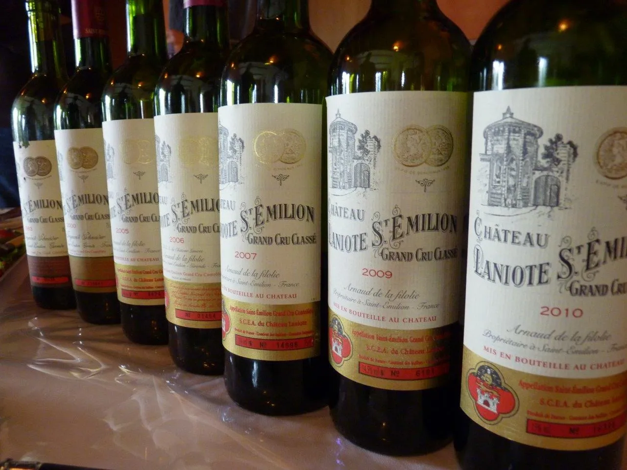 Collection of red wine bottles from Château Laniote, Bordeaux Grand Cru Classé, vintages 2007, 2009 and 2010, lined up on a white surface.
