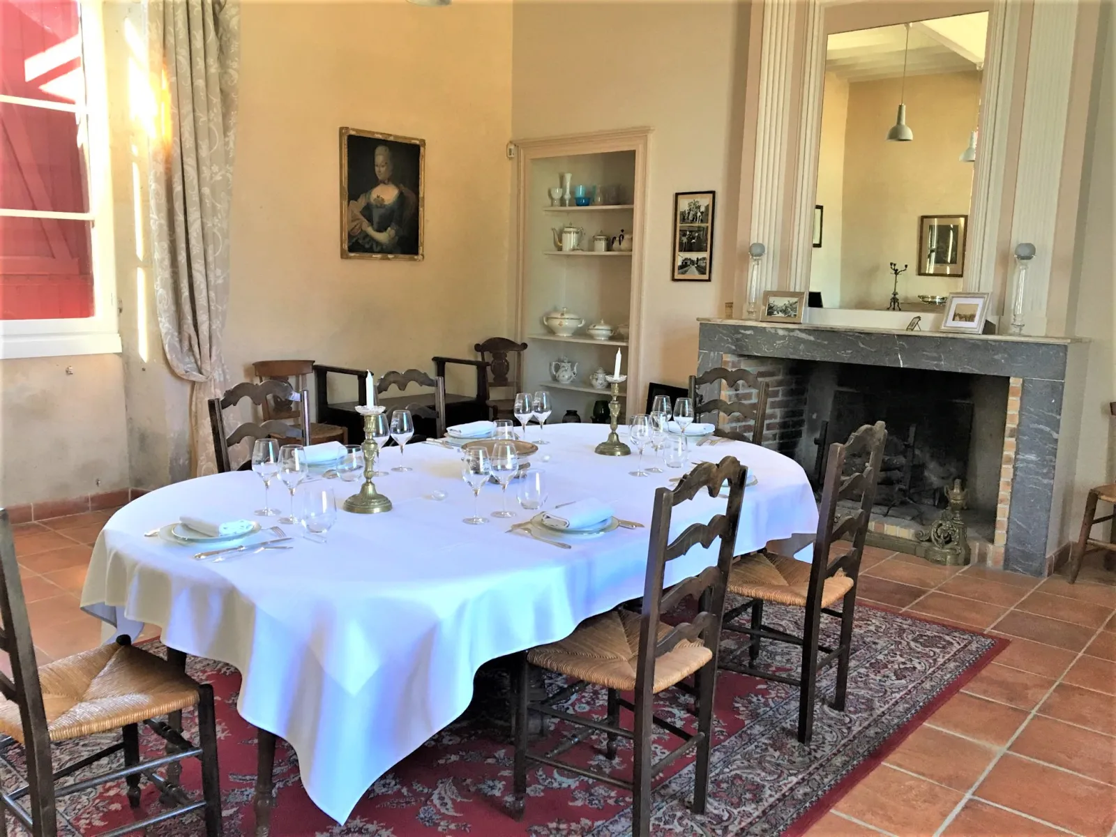Elegant dining room at Château Sigalas Rabaud featuring a round table set for service, wooden chairs, stone fireplace, antique portraits and classical Bordeaux furnishings.