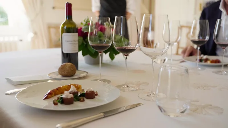 Wine tasting table in Bordeaux featuring lobster dish, red and white wine glasses, wine bottle and pink flowers in the background