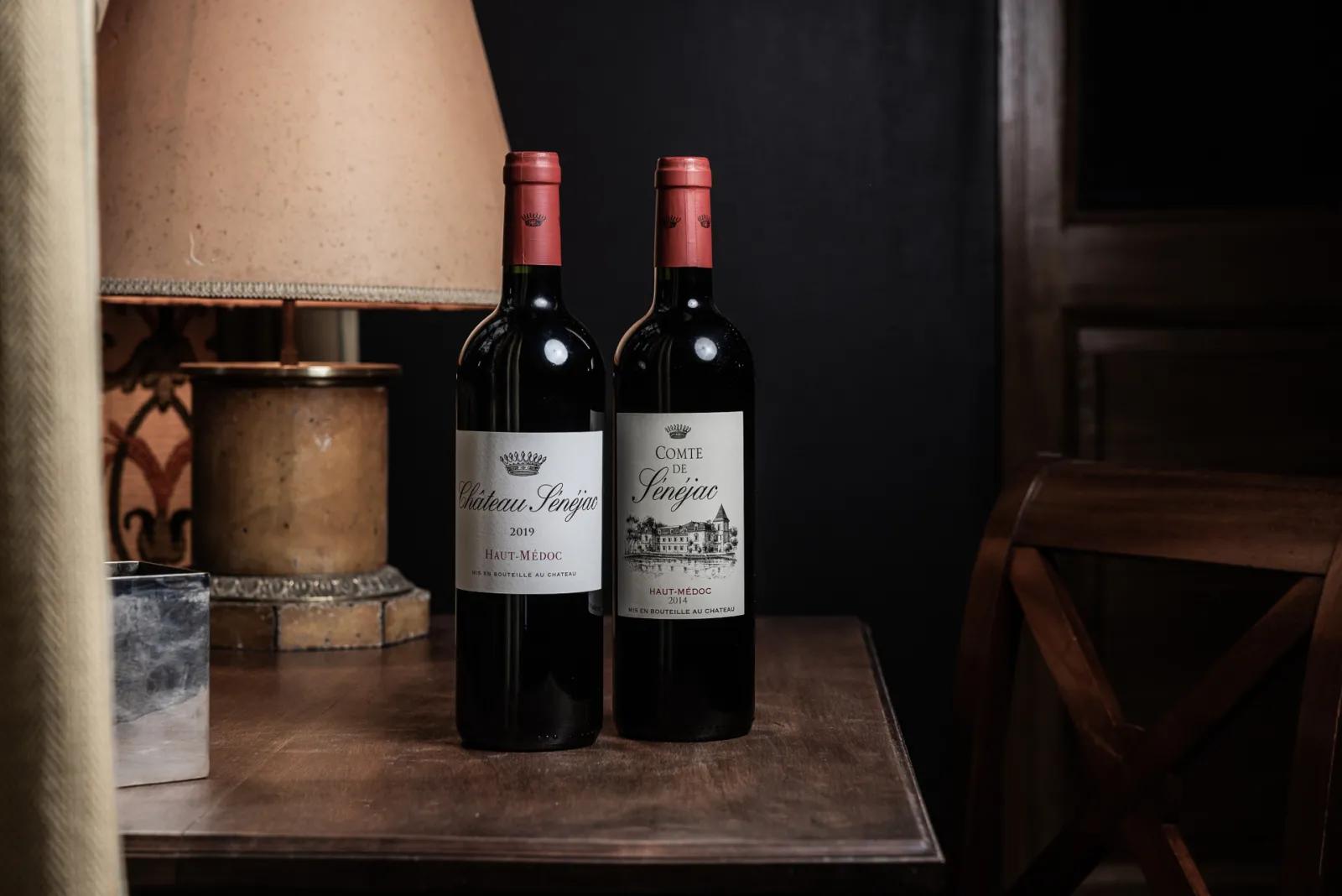 Two bottles of Haut-Médoc red wine from Château Sénéjac and Comte de Panjac displayed on a wooden table in an elegant setting.