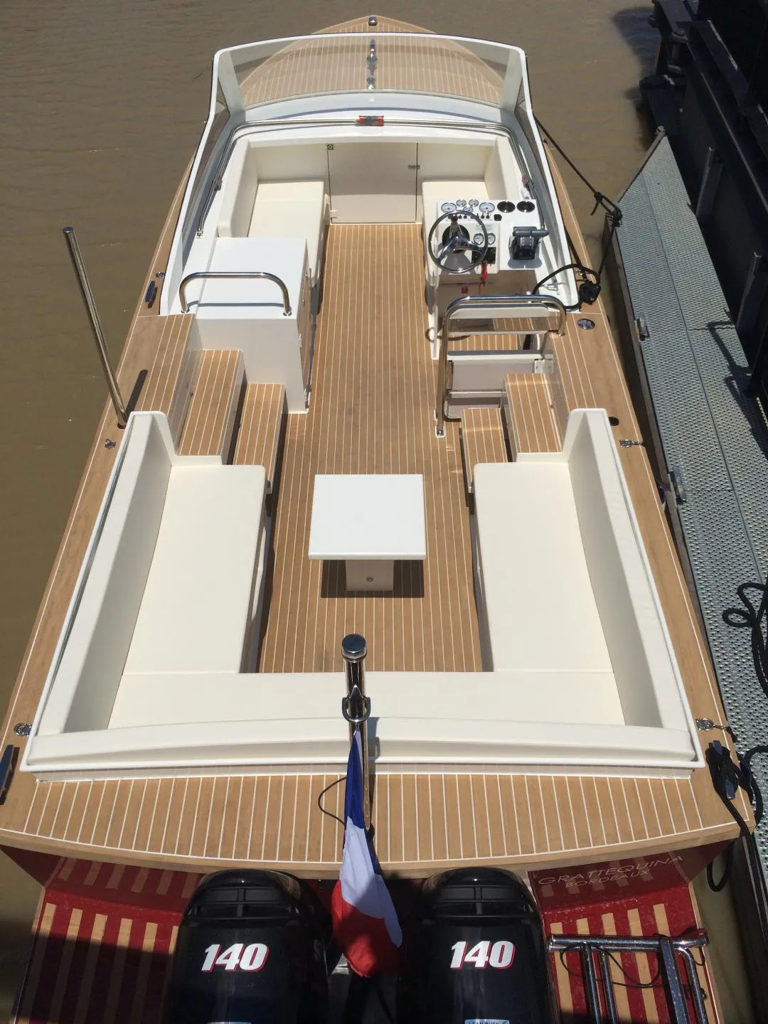 Overhead view of a white and wood taxi boat with twin 140 horsepower engines moored in Bordeaux, showing the deck, helm station, and passenger seating.