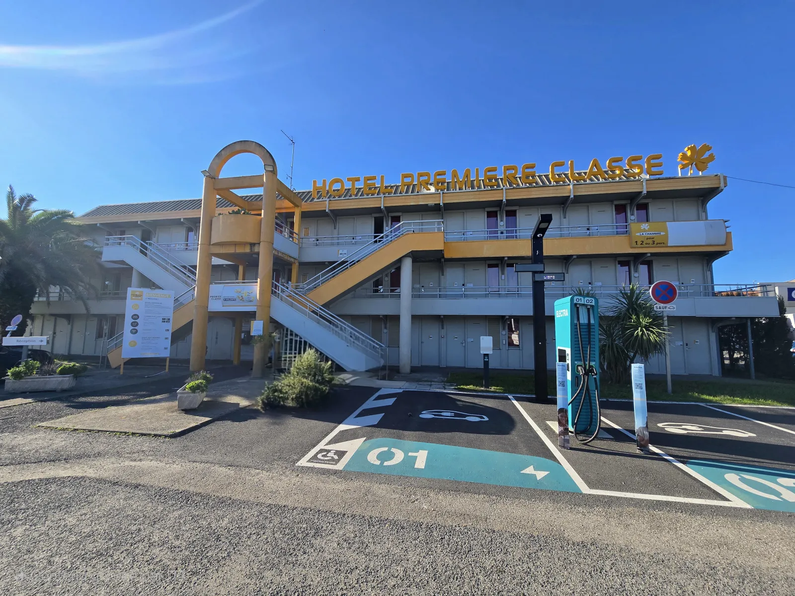 Première Classe Hotel Bordeaux West Eysines building exterior with golden signage, external staircase, and electric vehicle charging stations in the parking lot.