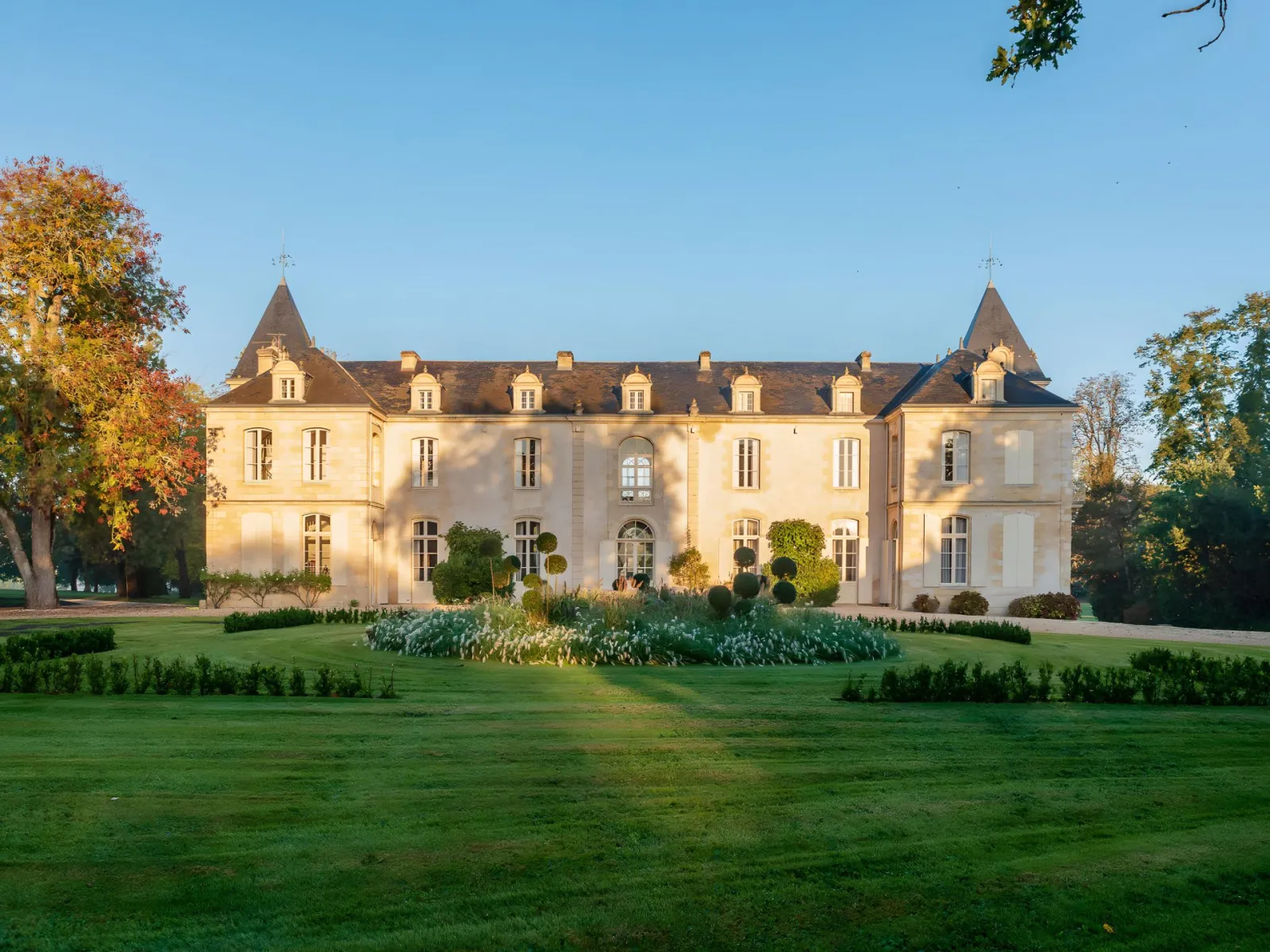 Château de Reignac near Bordeaux, an elegant neoclassical château featuring a cream-colored facade, pointed slate roofs with two towers, set in a verdant park with autumn foliage.