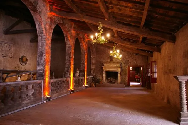 Interior of Château du Taillan in Bordeaux: large hall with stone vaults, illuminated gothic arches, golden chandelier, fireplace and terracotta floor.