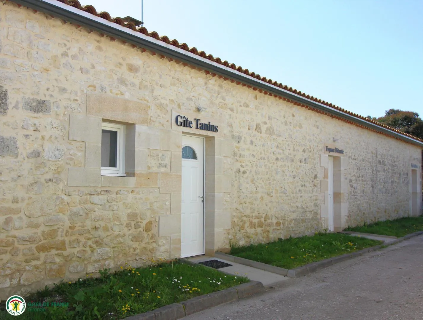 Beige stone facade of the Tanins guesthouse at Château Pierre de Montignac in Bordeaux, featuring a white door, window, and red tile roof