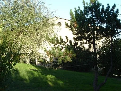 View of Château La Gontrie in Bordeaux with its white façade visible among trees, surrounded by green gardens and cypress trees.
