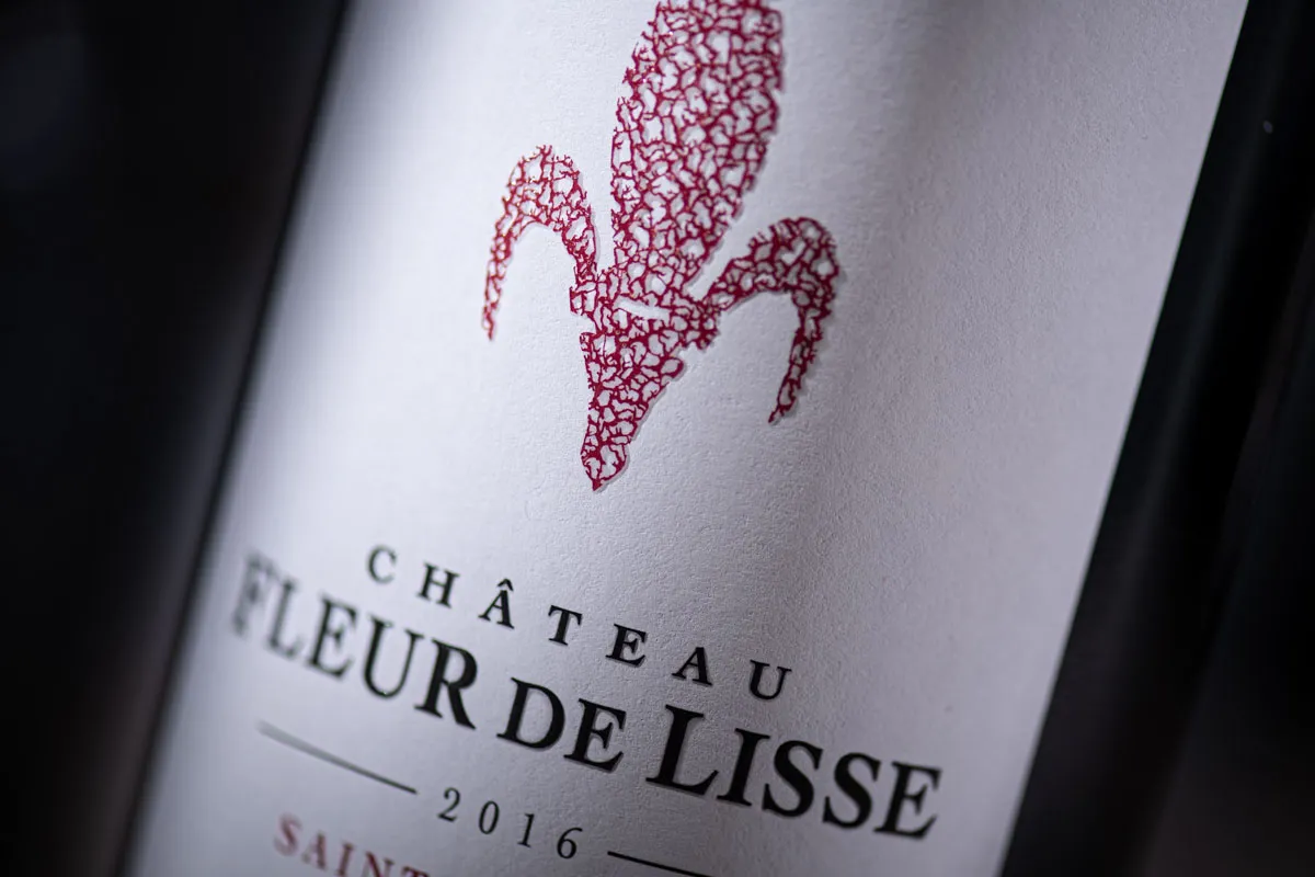 Red wine bottle label for Château Fleur de Lisse 2016 from Bordeaux, featuring a stylized red leaf design on a white background