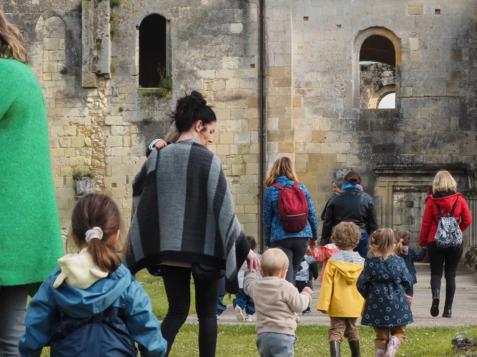 Group of children and adults touring the stone ruins of La Sauve-Majeure Abbey near Bordeaux, with medieval buildings featuring Romanesque arches in the background.