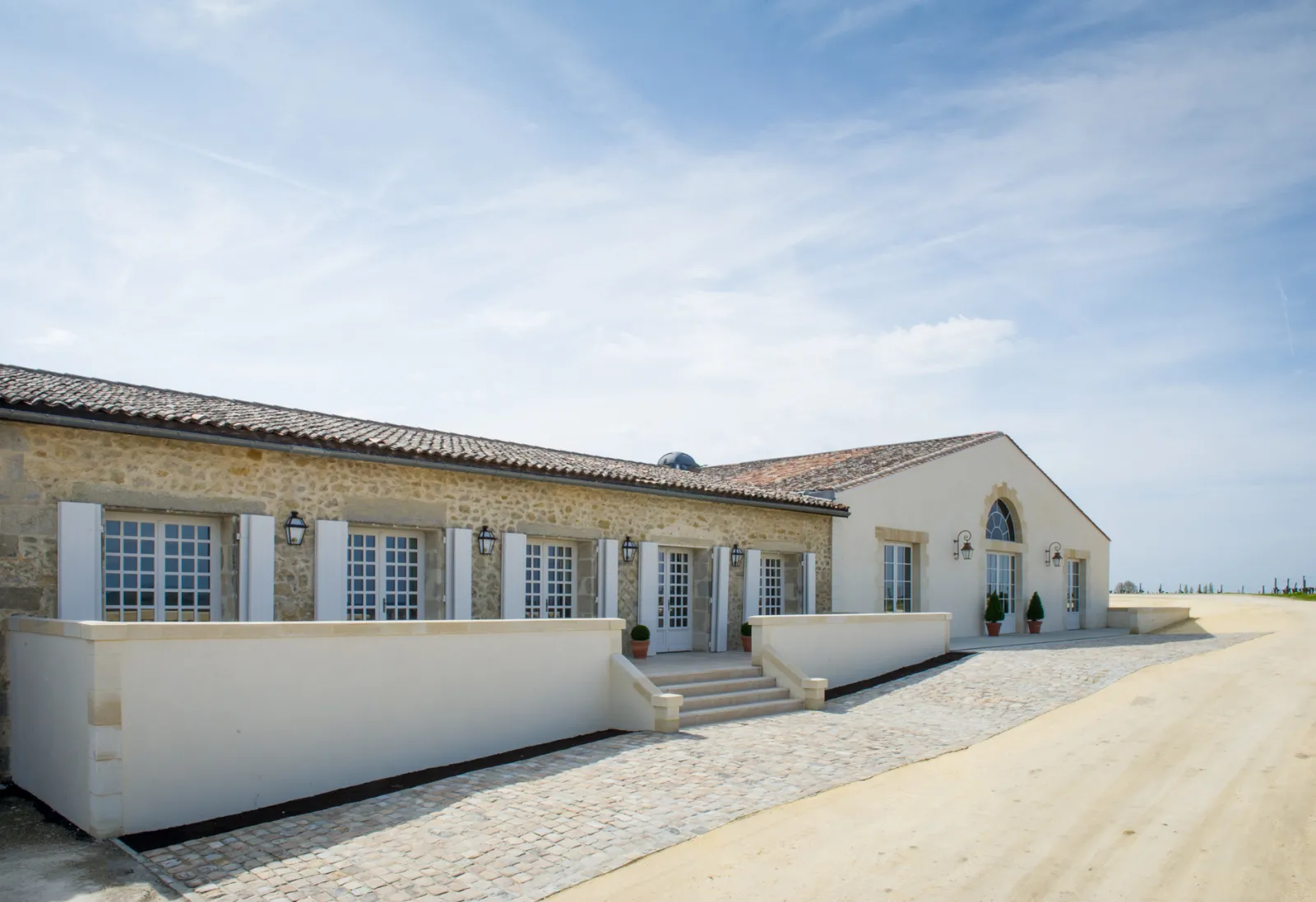 Front facade of Château de Rayne Vigneau in Bordeaux, stone building with white shutters, paved terrace and blue sky