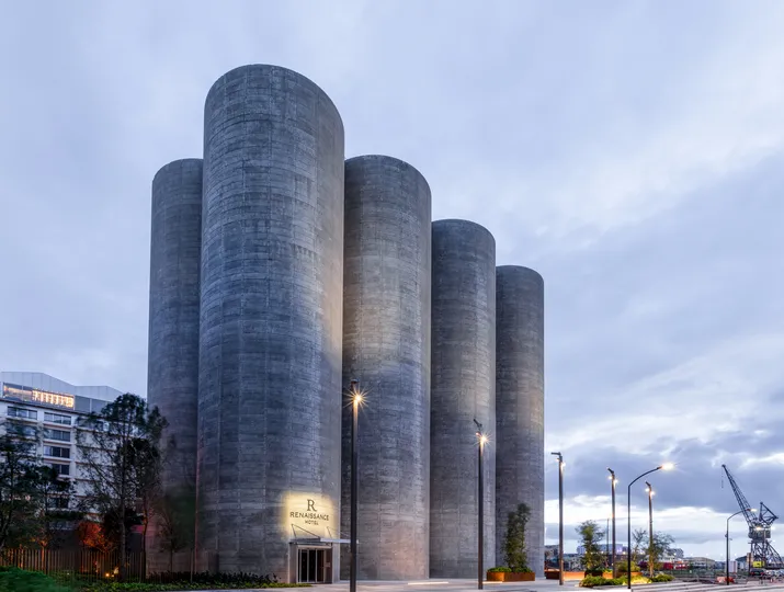Modern architectural facade of Renaissance Bordeaux Hotel featuring five vertical concrete cylinders in grey, lit up at dusk, located in Bordeaux's port district.