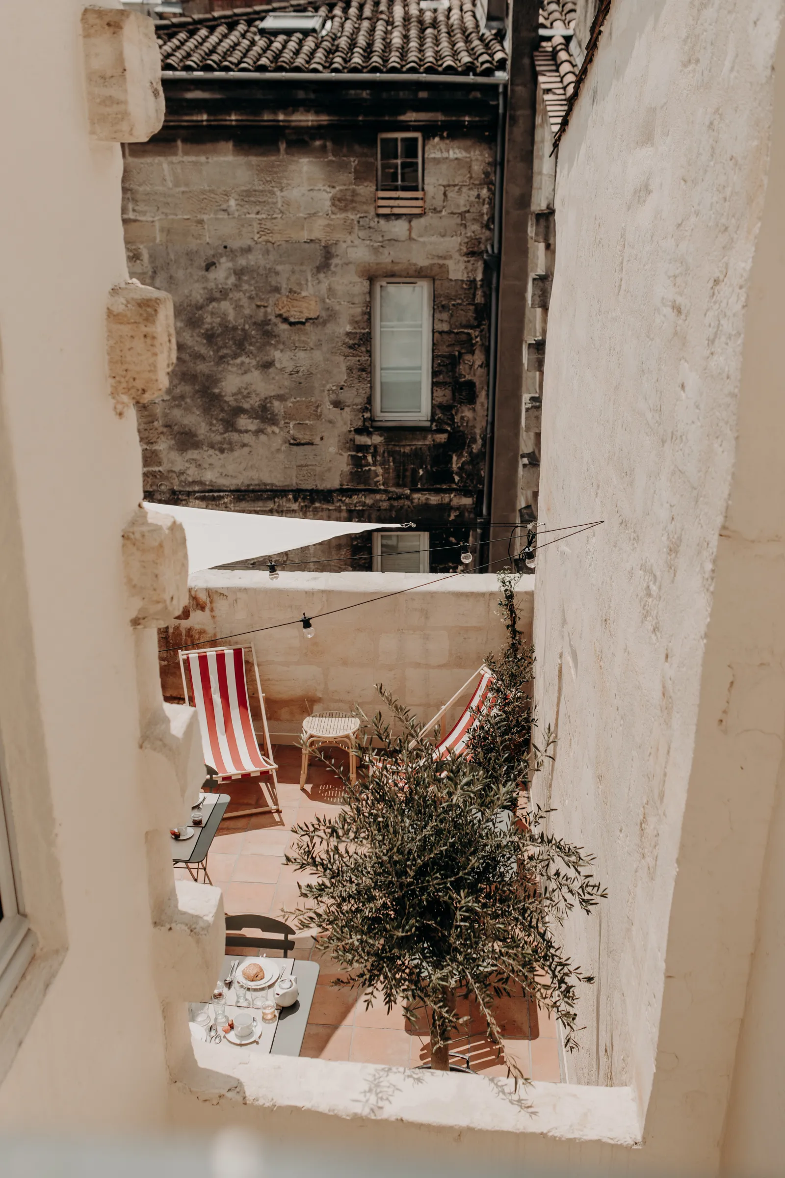 Overhead view of a small courtyard in Bordeaux featuring striped deck chairs, a potted green plant, hanging laundry, and old stone and brick buildings.