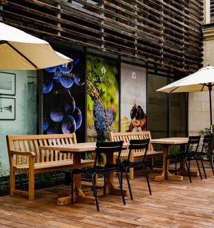 Restaurant terrace at Chais de la Fleur in Bordeaux featuring wooden tables and chairs, umbrellas, and decorative colorful murals on the walls.