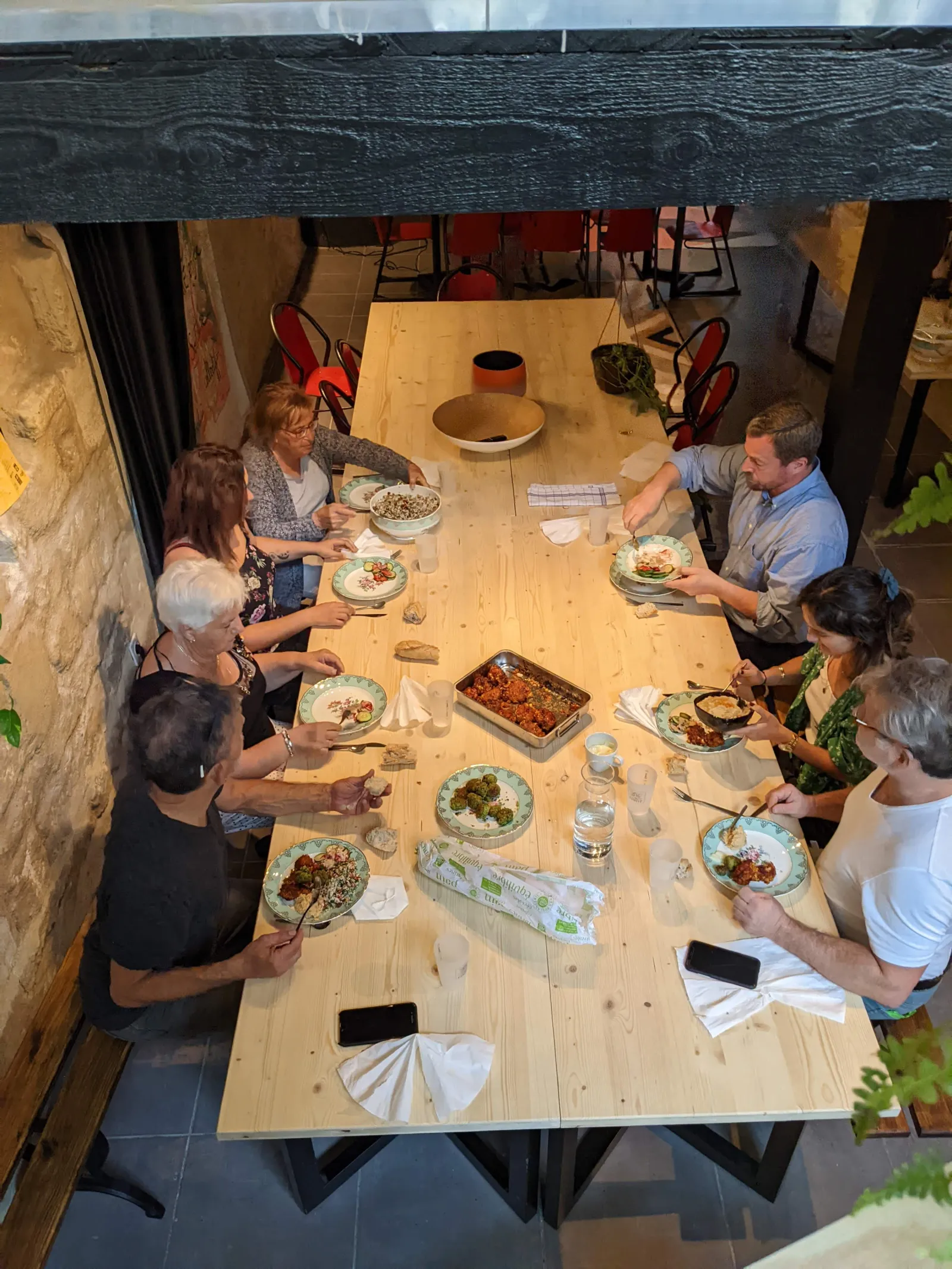 Overhead view of six people dining together at a wooden table in a Bordeaux restaurant, with plates of food and glasses of water on the table.