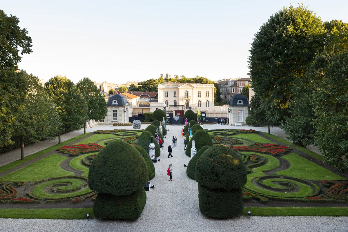 View of the courtyard at the Bernard Magrez Cultural Institute in Bordeaux featuring French formal gardens with manicured topiary and flower beds, and the main white building in the background