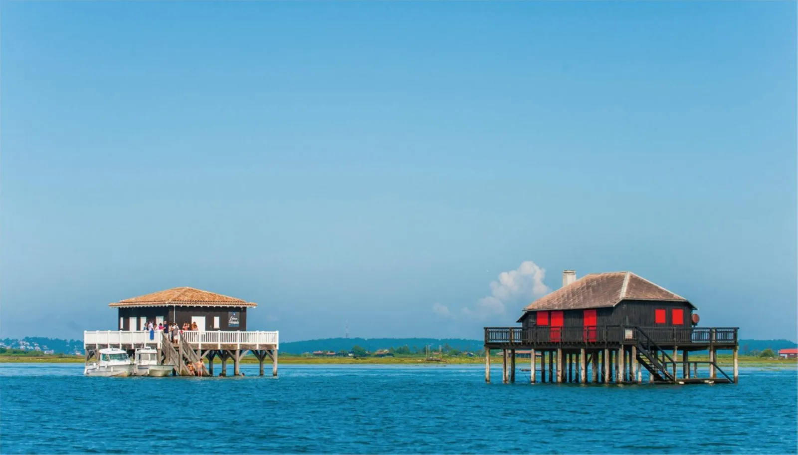 Two colorful stilt houses in turquoise water under a clear blue sky with landscape in the background