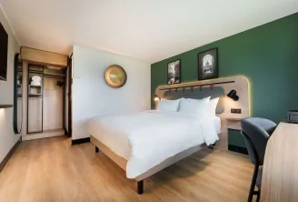 Modern hotel room at Campanile Nature Bordeaux Lac featuring a double bed with white linens, green accent wall, workspace, open wardrobe and contemporary bathroom