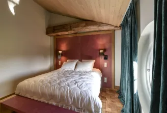 Elegant bedroom at Château Beauregard in Bordeaux featuring a queen-size bed with white linens, burgundy headboard, light wood ceiling with exposed beams, and green drapes.