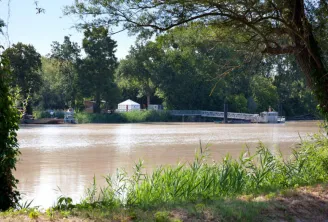 View of Île d'Arcins in Bordeaux with the swollen Garonne river, a white tent, and trees in the background