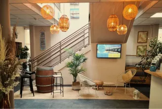 Modern reception hall of Bordeaux Blanquefort Youth Hostel featuring stairs, orange wicker pendant lights, rattan chairs, decorative plants and bar area.