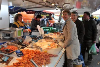 Fishmonger stall at Bassens market in Bordeaux displaying pink shrimp and fish, with smiling customers and sellers