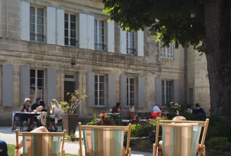 Three striped deckchairs on the lawn of Château Ambe Tour Pourret garden in Bordeaux, with visitors sitting in the background in front of the stone façade.