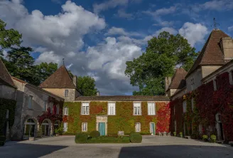 Courtyard of Château Carbonnieux in Bordeaux featuring ivy-covered stone buildings, pointed towers, and a clear blue sky