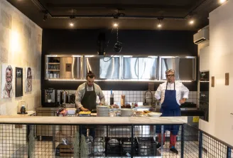 Two chefs work in a modern open kitchen at La Cuisine de Camille in Bordeaux, featuring illuminated display cases and cooking equipment.