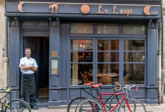 Storefront of Le Loup restaurant in Bordeaux with a waiter in professional attire at the entrance and red bicycles parked outside