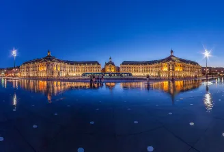 Night view of Place de la Bourse in Bordeaux with illuminated historic buildings reflected in the water mirror at twilight.