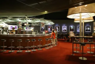 Interior of UGC Ciné Cité cinema in Bordeaux featuring a concession counter, bar stools, red carpet, illuminated portrait displays on walls, and waiting customers.