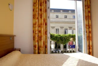 Hotel room overlooking the Bordeaux Opera House facade and interior courtyard, gold curtains, bed with beige bedspread