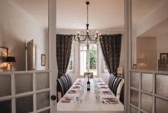 Elegant dining room at Château Ambe Tour Pourret in Bordeaux featuring a long formal table, wrought iron chandelier, brown curtains and glass doors with geometric panels