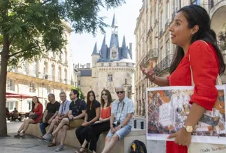 A group of tourists seated listening to a tour guide during a walking tour in Bordeaux, with historic buildings and a castle in the background.