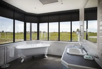 Luxury bathroom featuring a white freestanding bathtub, integrated sink, and panoramic windows overlooking Bordeaux vineyards