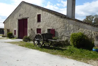 Stone building with burgundy doors and windows, wooden-wheeled cart in front of the facade, chimney in the background, Château de Lisennes near Bordeaux