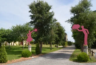 Park pathway with two bright pink sculptural figures playing, surrounded by trees and green spaces at Château Yon-Figeac in Bordeaux.