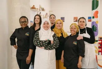 Team of Marie Curry restaurant in Bordeaux: seven smiling women posing together in a white space decorated with shelves and colorful artwork, some wearing the restaurant's black uniform.