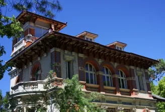 Belle Époque villa in Arcachon's Winter Town featuring red brick façade, arched windows, ornamental balustrades, and pitched roofs surrounded by vegetation.