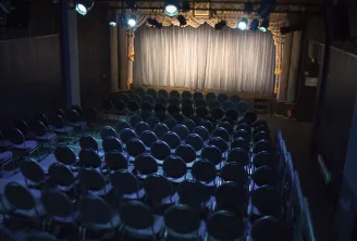 Empty theater auditorium with rows of black seats facing an illuminated stage with white and gold curtains in Bordeaux