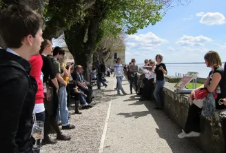 Group of visitors gathered on a paved path along the fortifications of Blaye Citadel, overlooking the Gironde estuary with century-old trees.