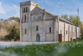 Basilica of Notre-Dame-de-la-fin-des-Terres in Bordeaux, stone church with square tower and Romanesque façade, surrounded by greenery under blue sky.